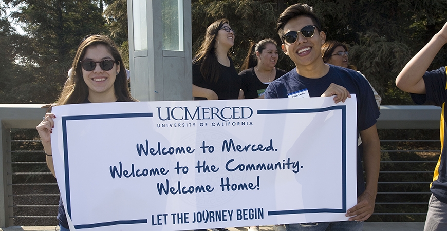 Two UC Merced students hold a sign that reads: "Welcome to Merced, welcome to the community, welcome home!"